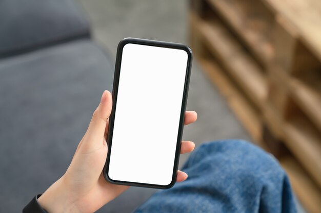 Hand, die Smartphone mit leerem Bildschirm auf dem Sofa hält