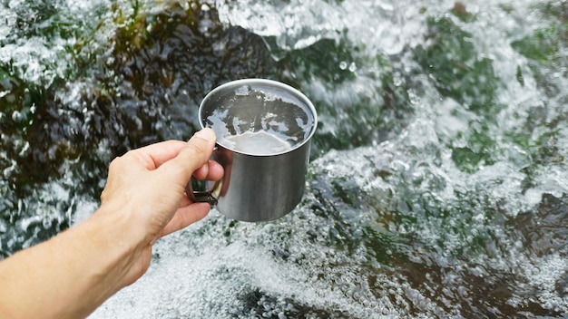 Hand, die Tasse mit Trinkwasser des reinen Wasserfalls hält