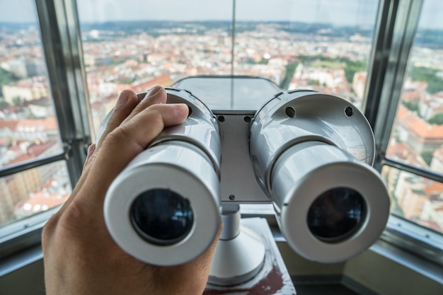 Hand, die Touristenfernglas und unscharfe Stadt auf Hintergrund im hohen Ansichtspunkt hält. Prag