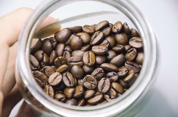 Hand, die transparentes Glasgefäß mit Kaffeebohnen hält