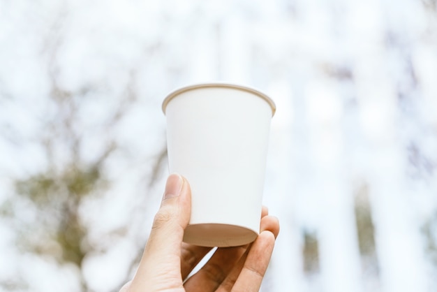 Hand, die weiße leere Kaffeetasse zum Mitnehmen Papier, Karton oder Pappe mit Unschärfe hält.