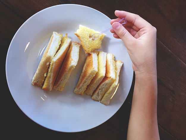 Hand, die Zuckerbutter-Brot auf weißer Kreisplatte auswählt