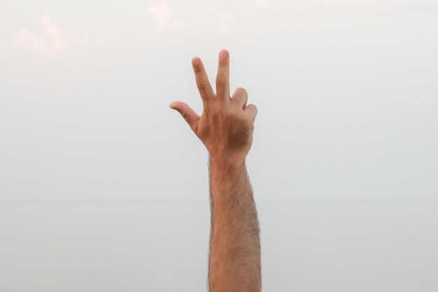 Foto hand doing showing number three gesture symbol on bright blue summer sky nature background gesturing number 3 number three in sign language third and counting three concepts 3 finger up