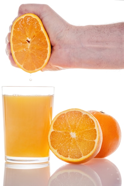 Hand drückte frischen Orangensaft in ein Glas, das auf weißer Wand isoliert wurde