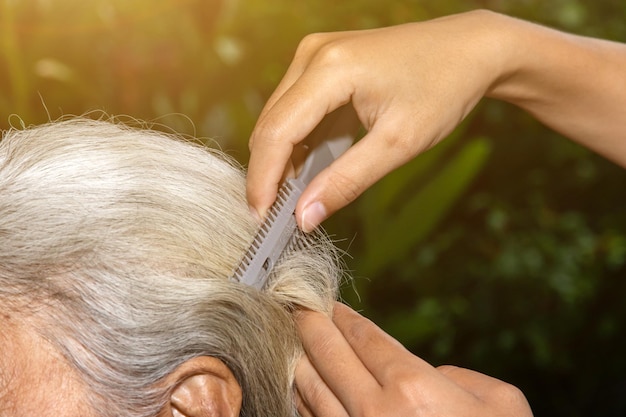 Hand einer Frau, die zu Hause die Haare ihrer älteren Mutter in der Natur schneidet