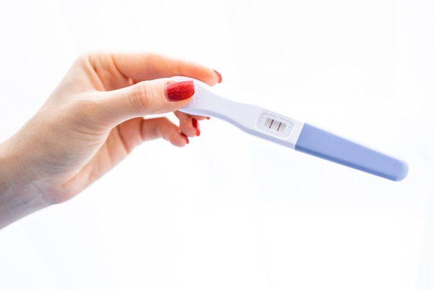 Hand einer jungen Frau hält einen Schwangerschaftstest mit zwei Streifen auf weißem Hintergrund Positives Ergebnis Nahaufnahme