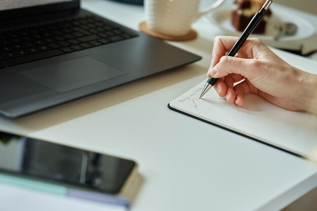 Hand einer nicht erkennbaren Person zeichnet Skizze auf Papier sitzt zu Hause an seinem Schreibtisch mit Laptop vor o