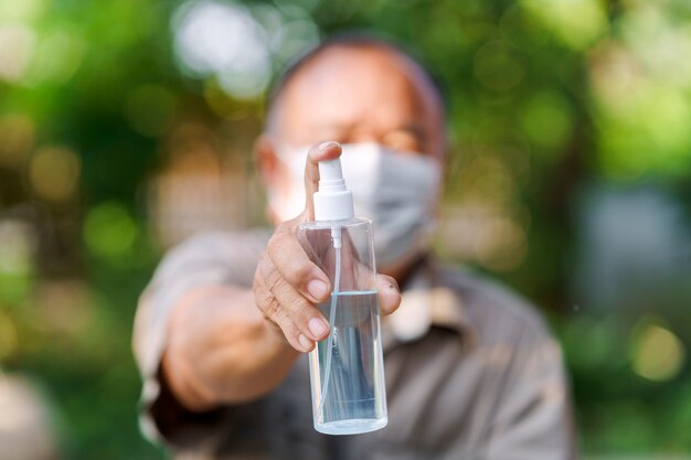 Hand eines alten Mannes, der eine Maske trägt und eine Alkoholsprühflasche hält Hygienekonzept