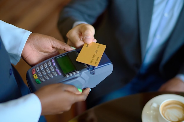 Hand eines jungen Geschäftsmannes, der eine Kreditkarte über einem Zahlungsterminal hält