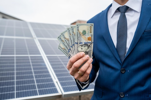 Hand eines jungen Mannes, der Dollar für die Installation neuer Sonnenkollektoren hält