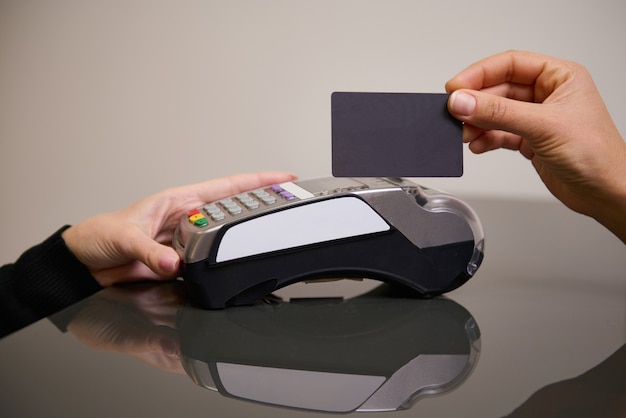 Hand eines Kunden, der mit einer kontaktlosen Kreditkarte mit NFC-Technologie bezahlt. Spa-Administrator mit Kreditkartenleser an der Rezeption mit einer Frau, die eine Kreditkarte hält. Near Field Communications
