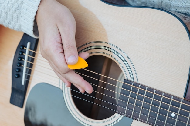 Hand eines Mädchens, das einen orangefarbenen Mediator in der Hand hält und Gitarre spielt, in der Nähe des Konzepts des Musikspels und des Übens