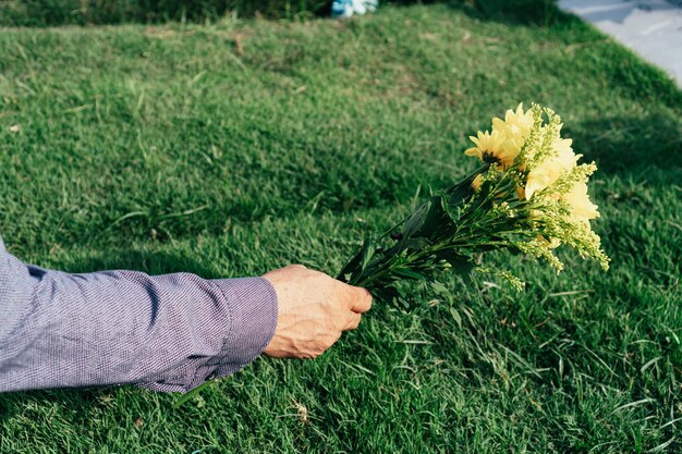 Hand eines Mannes, der auf einem Friedhof Blumen auf das Grab legt
