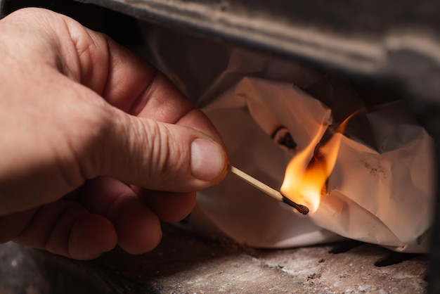 Hand eines Mannes, der brennendes Streichholz hält und Feuer im Festbrennstoffkessel macht Hausheizungswärme zu Hause während der kalten Jahreszeit