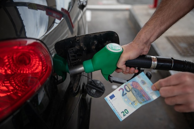 Hand eines Mannes, der das Auto betankt und ein 20-Banknoten-Konzept steigender Kraftstoffpreise hält