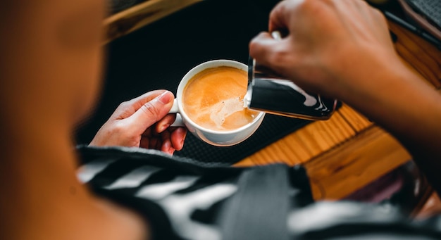 Hand eines professionellen Baristas, der gedämpfte Milch in die Kaffeetasse gießt und so einen Latte macht