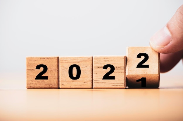 Hand Flipping Holzblockwürfel zwischen 2021 und 2022 mit Bokeh-Hintergrund für Veränderung und Vorbereitung Frohe Weihnachten und ein glückliches neues Jahr.