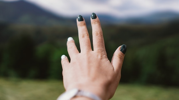 Hand gegen Berg. Weibliche Hand vorwärts. Bergtal. Natürliche Sommerlandschaft.