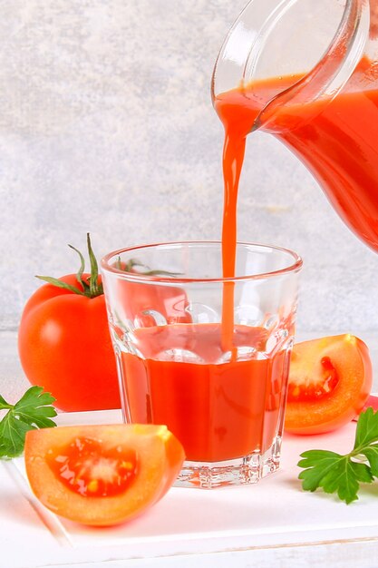 Hand gegossener Tomatensaft von einem Pitcher in ein Glas auf einer grauen konkreten Tabelle.