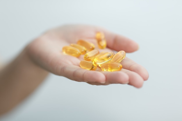 Hand gibt Kapseln Omega 3 auf weißem Hintergrund. Handfläche nach oben, Nahaufnahme. Hochauflösendes Produkt. Gesundheitskonzept.