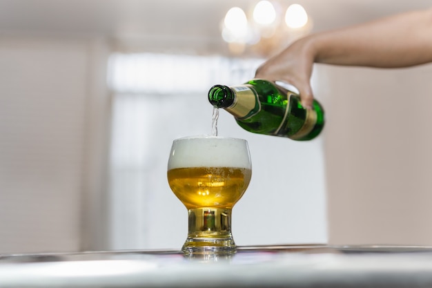 Hand gießt Bier aus grüner Flasche in Glas.