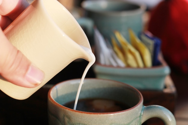 Hand gießt Milch in Tasse Kaffee