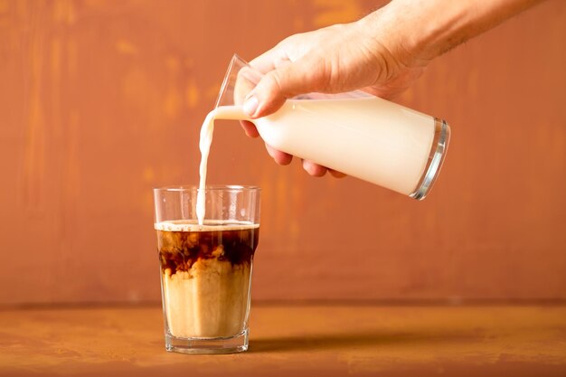 Hand gießt Milch zu gebrühtem Kaffee im Studio mit Kopienraum