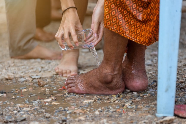 Hand gießt Wasser auf den Fuß der verehrten Ältesten und bittet um Segen glücklich