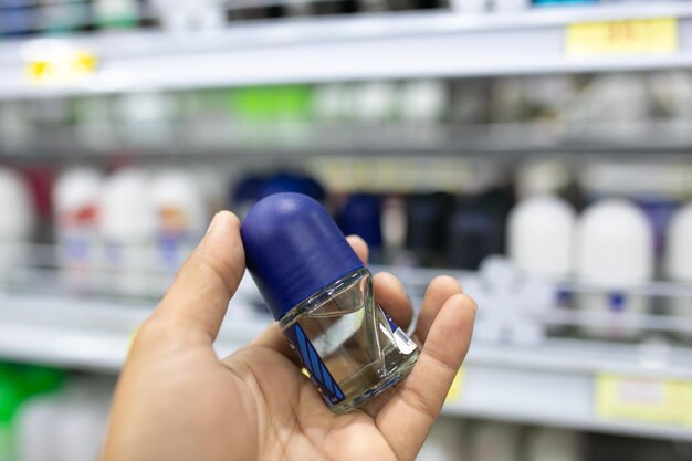 Hand hält Deo-Flasche auf dem Regal im Supermarkt, verschwommener Hintergrund