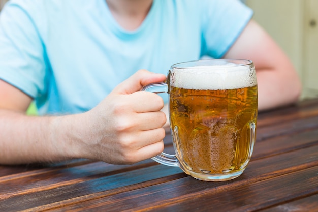 Hand hält ein Glas Bier auf Holztisch