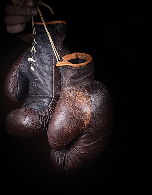 Hand hält ein Paar braune sehr alte Boxhandschuhe