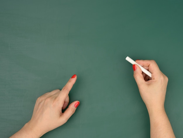 Hand hält ein Stück weiße Kreide auf dem Hintergrund einer leeren grünen Kreidetafel, Präsentation