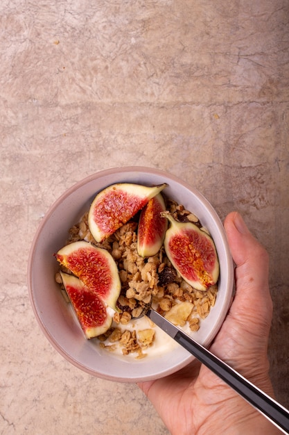 Hand hält eine Schüssel mit Joghurt, Müsli, Feigenplatz für Text