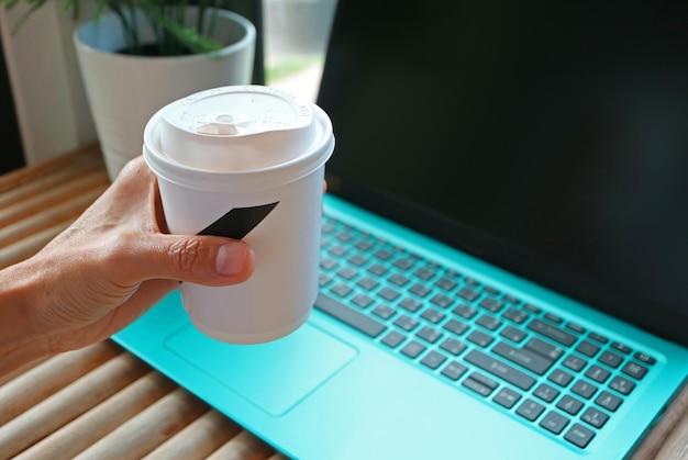 Hand hält eine Tasse Getränk mit Laptop im Hintergrund