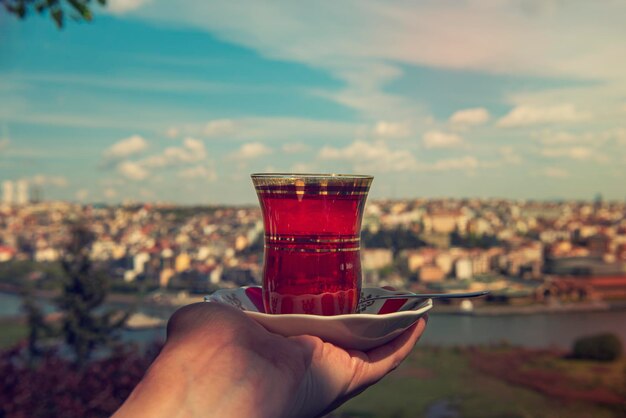 Hand hält eine Tasse traditionellen türkischen Tee gegen den Blick auf Istanbul, Türkei