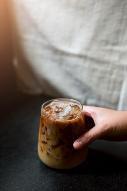 Hand hält einen Eiskaffee zum Mitnehmen auf schwarzem Tisch