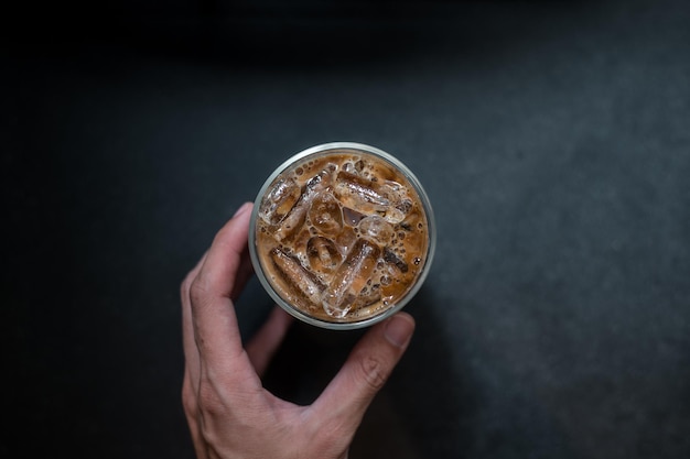 Hand hält einen Eiskaffee zum Mitnehmen auf schwarzem Tisch