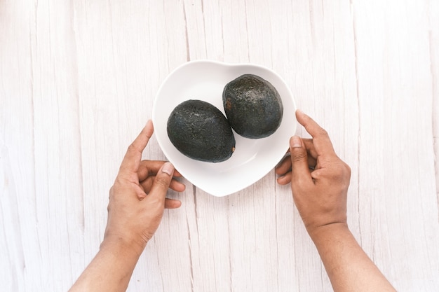 Hand hält einen Teller Avocado auf Holztisch