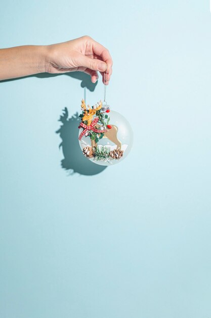 Hand hält einen Weihnachtsbaumschmuck auf blauem Hintergrund. Hartes Licht.