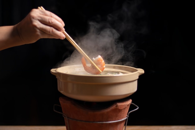 Hand hält Essstäbchen mit Garnelen über Hot Pot Thai Art.