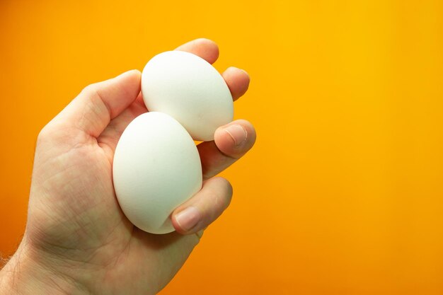 Hand hält gekochte Eier auf einem orangefarbenen Hintergrund