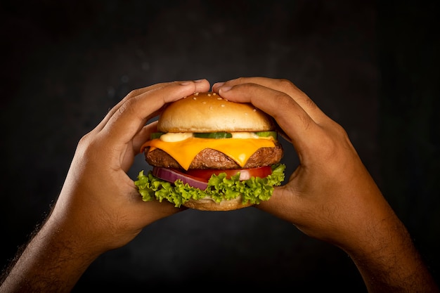 Hand hält Hamburger auf dunklem Hintergrund