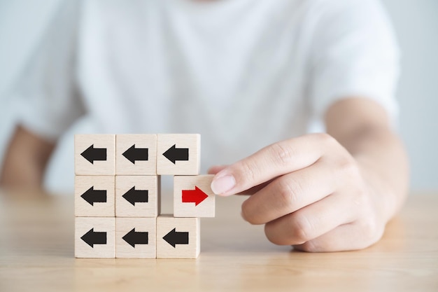 Hand hält Holzblock mit rotem Pfeil in die entgegengesetzte Richtung schwarze Pfeile Einzigartig Denken Sie anders Individuell und heben Sie sich von der Masse ab conceptxA