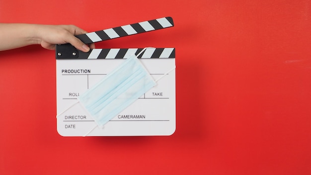 Hand hält Klappe oder Filmtafel mit Gesichtsmasken in der Kinoindustrie auf rotem Hintergrund