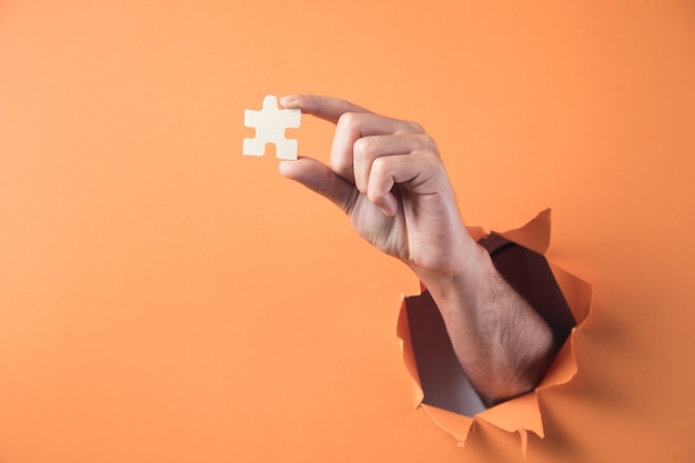 Hand hält Puzzleteil auf orange Hintergrund