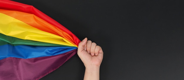 Hand hält Regenbogenflagge auf schwarzem Hintergrund.