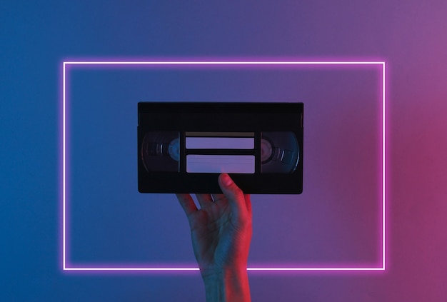 Hand hält Retro-Videokassette mit rotem blauem Neonlicht.