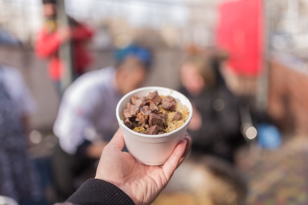 Hand hält Schüssel mit Fleisch und Reis.