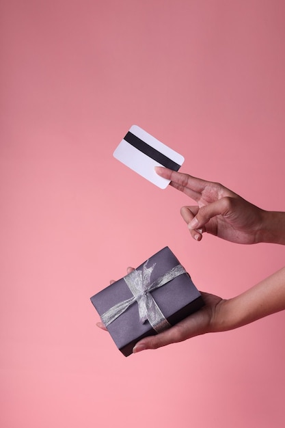 Hand hält schwarze Geschenkbox mit silbernem Band und Einkaufskarte isoliert auf rosa Pastellhintergrund.