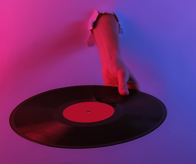 Hand hält Vinylplatte durch zerrissenes Loch. Kreative Pop-Art-Rosa-Blau-Neonfarbe. Trendige Farbverlaufsbeleuchtung. Nachtlicht